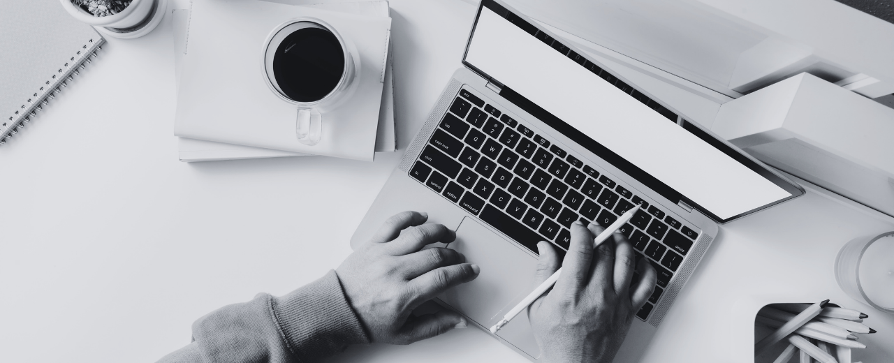 Person working at a clean, organized desk with a laptop, coffee, and stationery, focused on creativity and productivity.